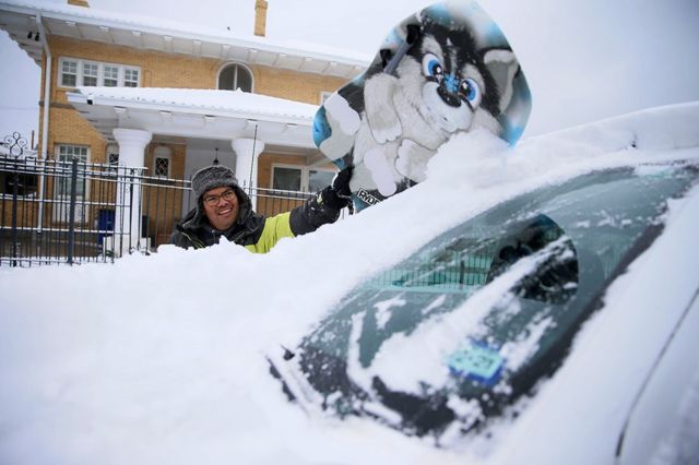A man clears snow from his windscreen