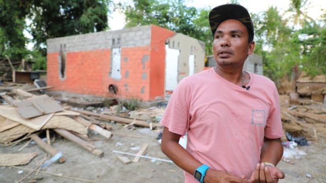 Damar in front of ruins that once his home