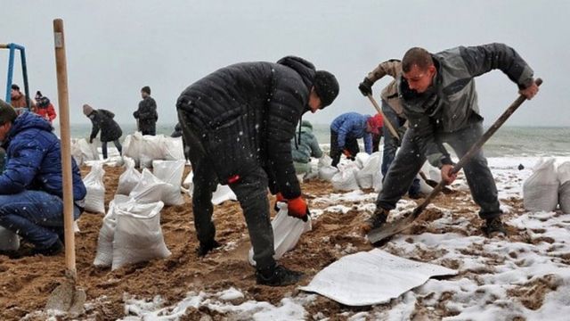 People filling up bags of sand on a beach.